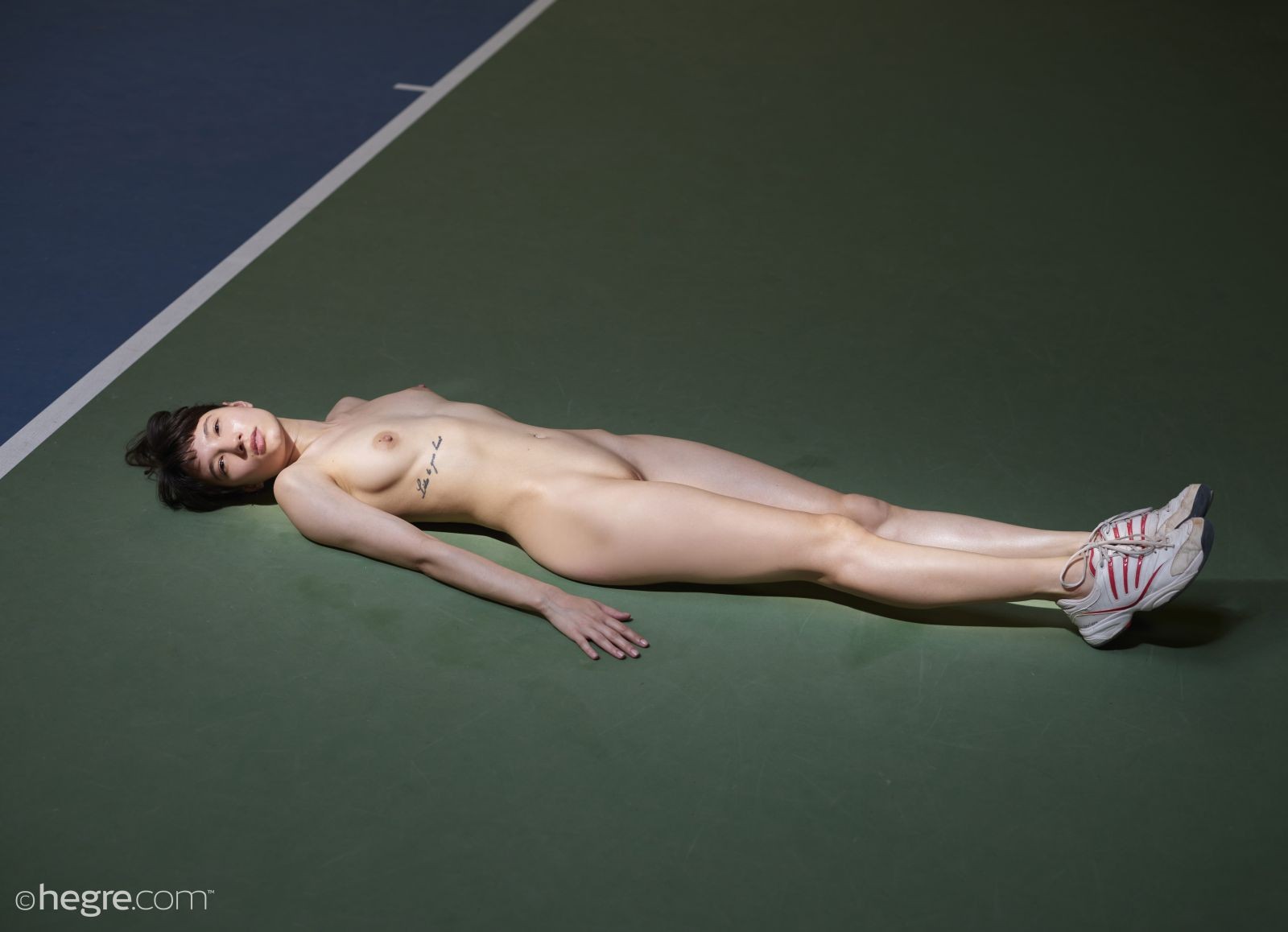 Голая спортсменка в кроссовках лежит на полу - фото